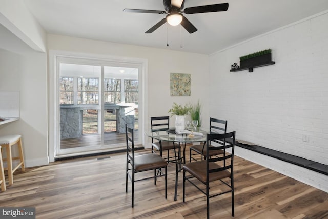 dining space featuring brick wall, baseboards, ceiling fan, and wood finished floors