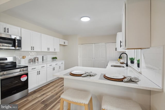 kitchen featuring stainless steel appliances, white cabinetry, a sink, and a peninsula