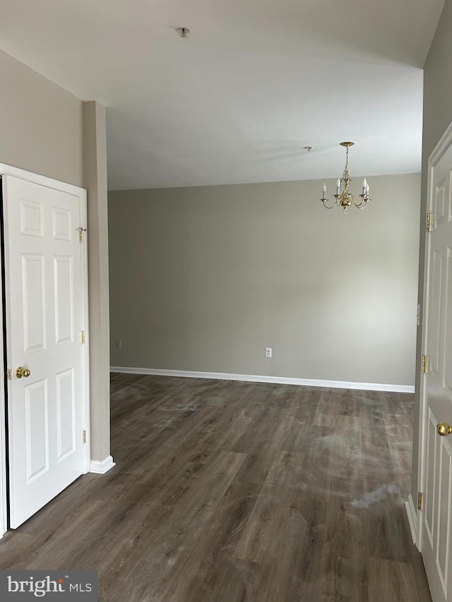 spare room with an inviting chandelier and dark hardwood / wood-style floors