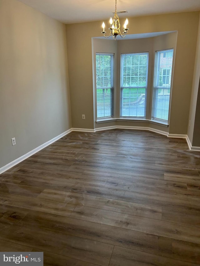 empty room featuring an inviting chandelier and dark hardwood / wood-style floors