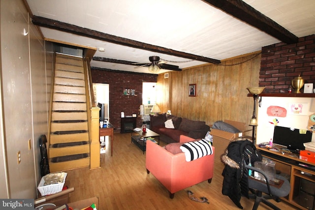 living room featuring hardwood / wood-style flooring, ceiling fan, beam ceiling, a fireplace, and brick wall