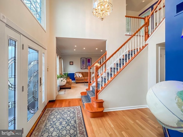 entrance foyer featuring crown molding, a towering ceiling, a notable chandelier, and light hardwood / wood-style flooring