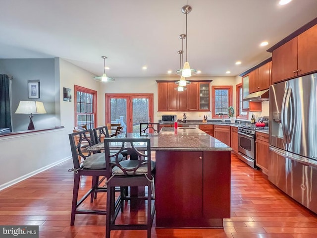 kitchen featuring appliances with stainless steel finishes, a kitchen island with sink, pendant lighting, and light stone counters