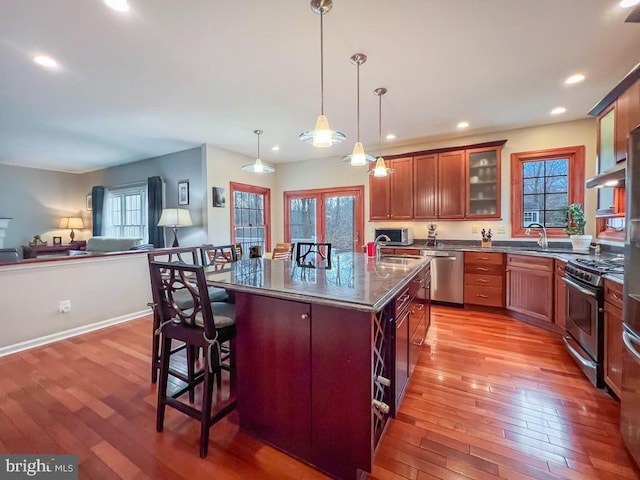 kitchen featuring appliances with stainless steel finishes, a kitchen bar, dark stone counters, hanging light fixtures, and a center island with sink