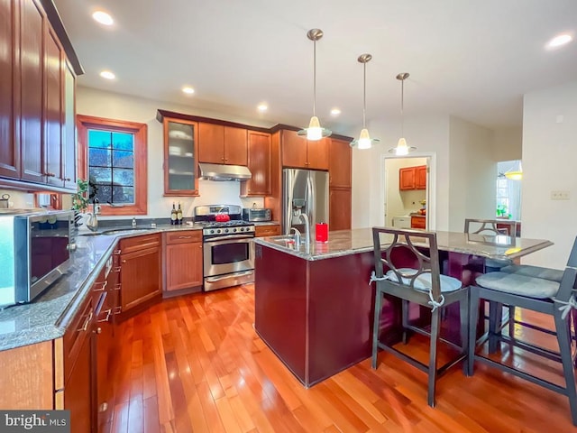 kitchen with a breakfast bar, an island with sink, hanging light fixtures, light stone counters, and stainless steel appliances