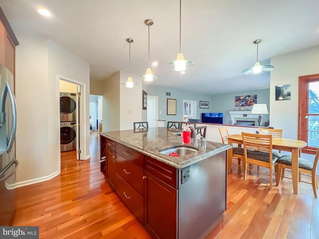 kitchen with decorative light fixtures, sink, a kitchen island with sink, stacked washer / drying machine, and light stone countertops