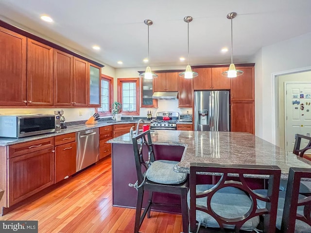 kitchen with hanging light fixtures, dark stone countertops, appliances with stainless steel finishes, and a center island with sink