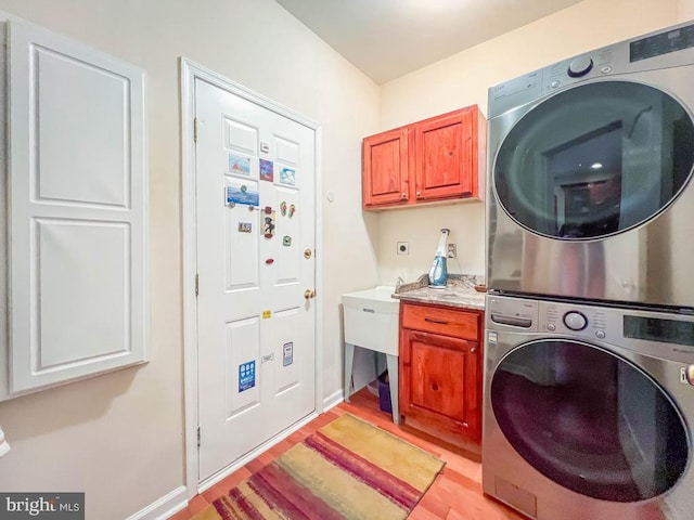 laundry area featuring cabinets, stacked washer and dryer, and light wood-type flooring