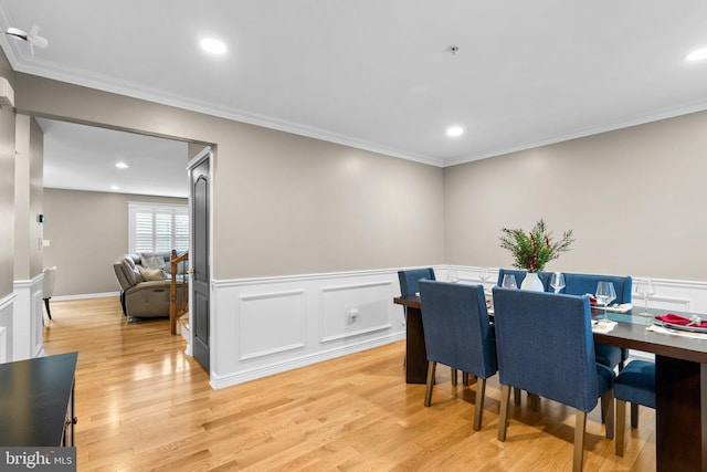 dining area featuring light wood-style floors, ornamental molding, and wainscoting