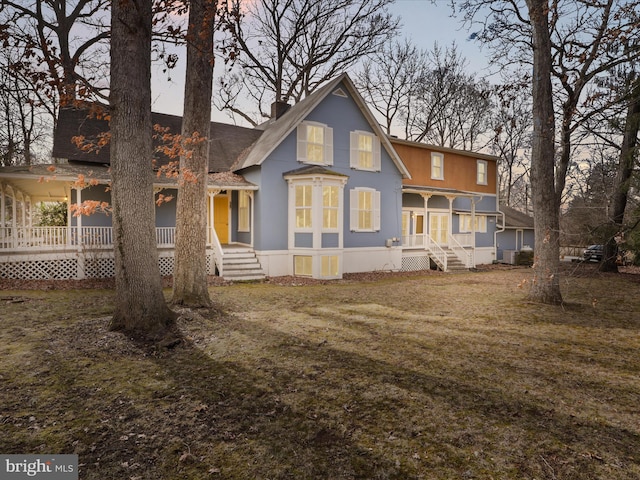 back of house featuring a chimney, a porch, and a yard