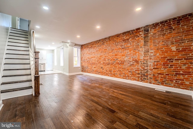 unfurnished living room with brick wall and dark hardwood / wood-style floors