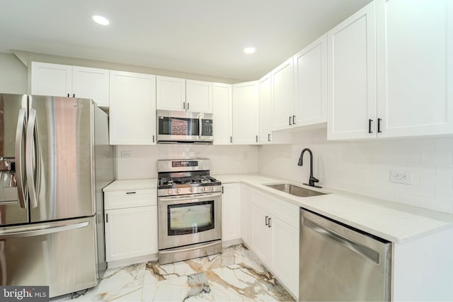 kitchen with appliances with stainless steel finishes, tasteful backsplash, white cabinetry, sink, and light stone counters