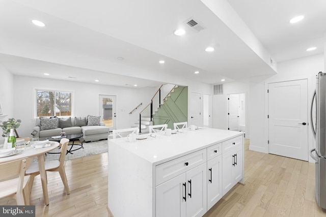 kitchen featuring light wood finished floors, white cabinets, a kitchen island, open floor plan, and light countertops