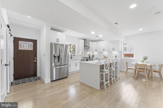 kitchen featuring a center island, stainless steel appliances, light countertops, white cabinetry, and wall chimney exhaust hood
