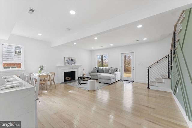 living room with stairs, light wood finished floors, a fireplace with flush hearth, and visible vents