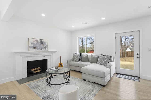 living area featuring visible vents, baseboards, light wood-style flooring, a brick fireplace, and recessed lighting