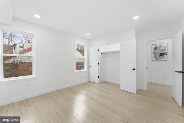 unfurnished bedroom featuring light wood-style flooring, multiple windows, and baseboards