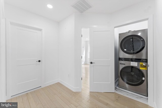 washroom with stacked washer and dryer, laundry area, light wood finished floors, baseboards, and visible vents