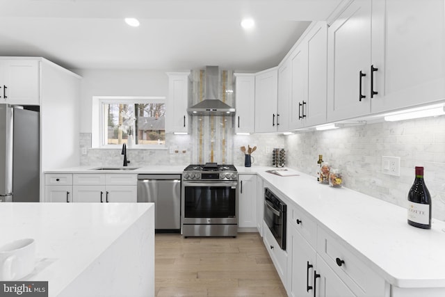 kitchen featuring wall chimney exhaust hood, appliances with stainless steel finishes, light wood-type flooring, white cabinetry, and a sink