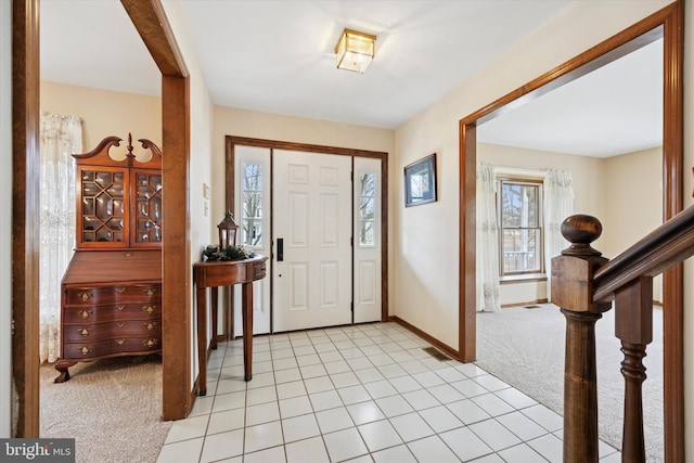 entrance foyer with light tile patterned flooring, light colored carpet, baseboards, and stairs