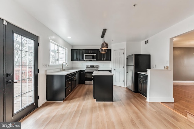 kitchen with a kitchen island, pendant lighting, sink, stainless steel appliances, and light wood-type flooring