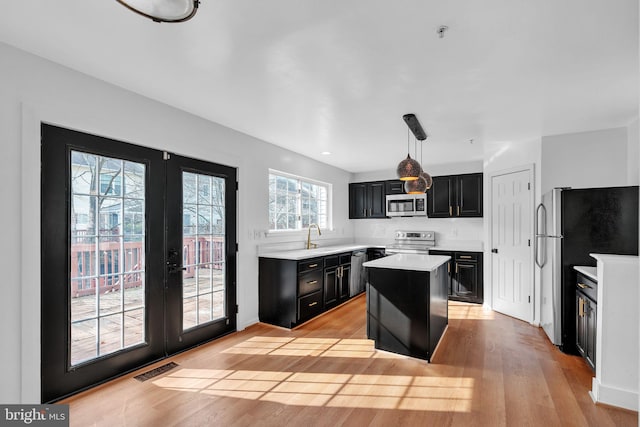 kitchen featuring light hardwood / wood-style flooring, hanging light fixtures, a center island, stainless steel appliances, and french doors