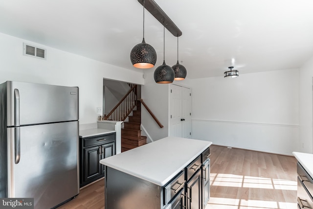 kitchen with decorative light fixtures, light hardwood / wood-style flooring, stainless steel refrigerator, and a kitchen island