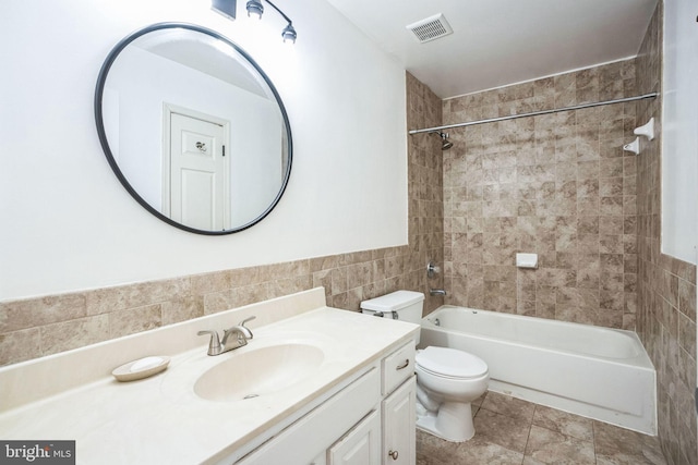 full bathroom featuring toilet, tiled shower / bath, tile walls, vanity, and tile patterned flooring