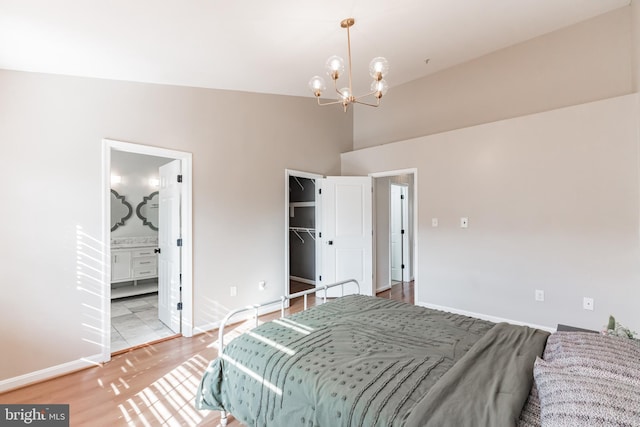 bedroom featuring vaulted ceiling, ensuite bathroom, a chandelier, and light hardwood / wood-style flooring