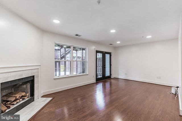 unfurnished living room with a tiled fireplace, dark hardwood / wood-style flooring, and french doors