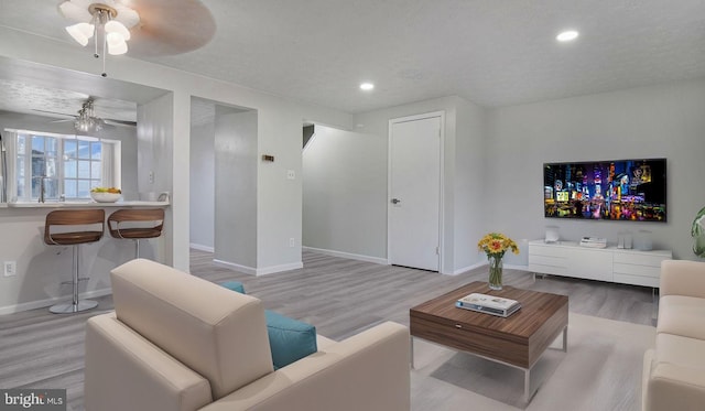 living room with ceiling fan, light hardwood / wood-style flooring, and a textured ceiling