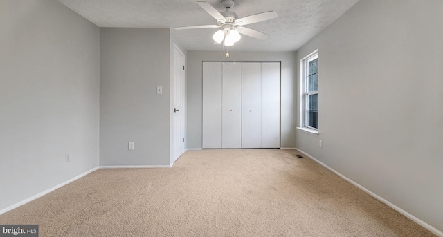 unfurnished bedroom with ceiling fan, a closet, light carpet, and a textured ceiling