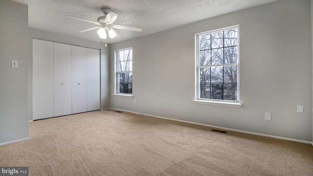 unfurnished bedroom with ceiling fan, light colored carpet, a closet, and a textured ceiling