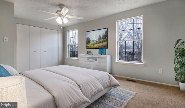 carpeted bedroom featuring ceiling fan, a closet, and a textured ceiling