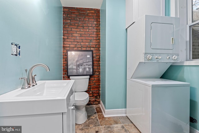 bathroom featuring stacked washing maching and dryer, vanity, and toilet