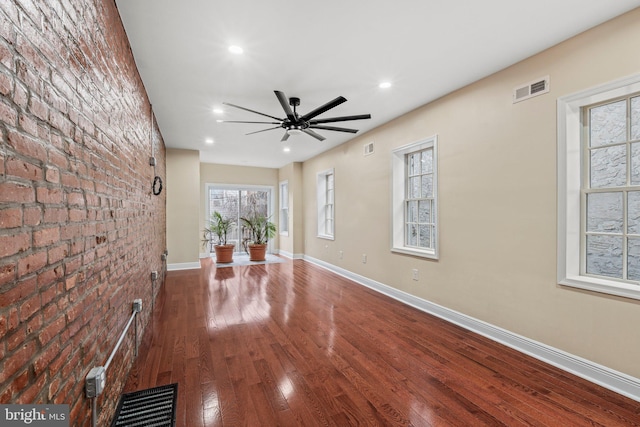 unfurnished living room featuring hardwood / wood-style flooring, ceiling fan, and brick wall