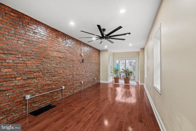 unfurnished living room with ceiling fan, brick wall, and wood-type flooring