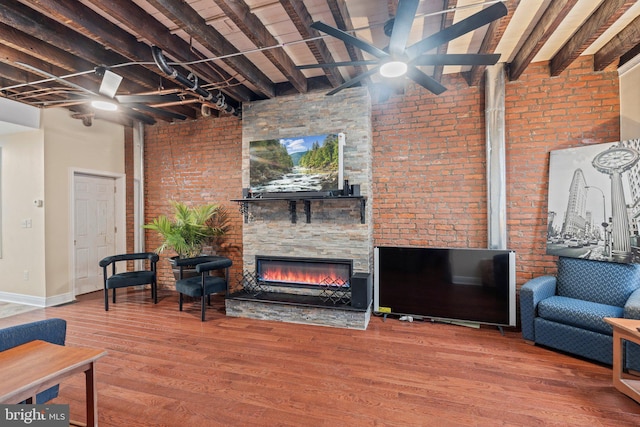 living room featuring wood-type flooring, beam ceiling, a stone fireplace, and a high ceiling