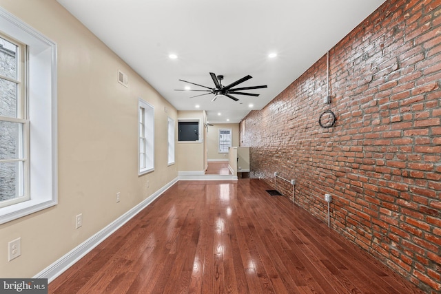 unfurnished living room featuring hardwood / wood-style floors, ceiling fan, and brick wall