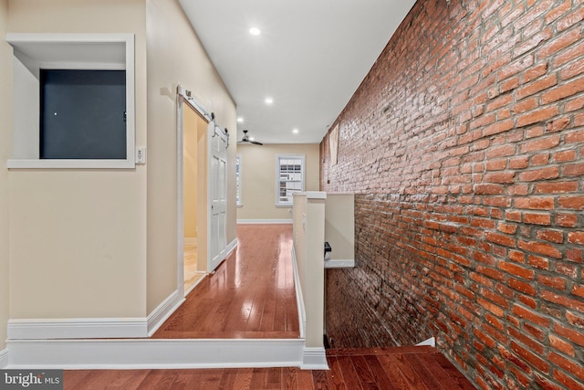 hallway with brick wall, wood-type flooring, and a barn door