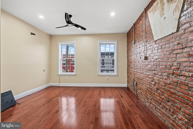 unfurnished room with ceiling fan, brick wall, and wood-type flooring