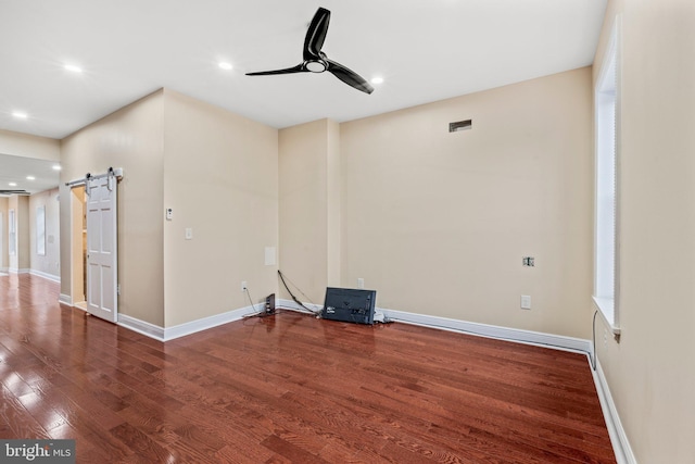 unfurnished room with ceiling fan, wood-type flooring, and a barn door