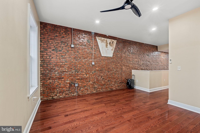 interior space with dark hardwood / wood-style flooring, ceiling fan, and brick wall