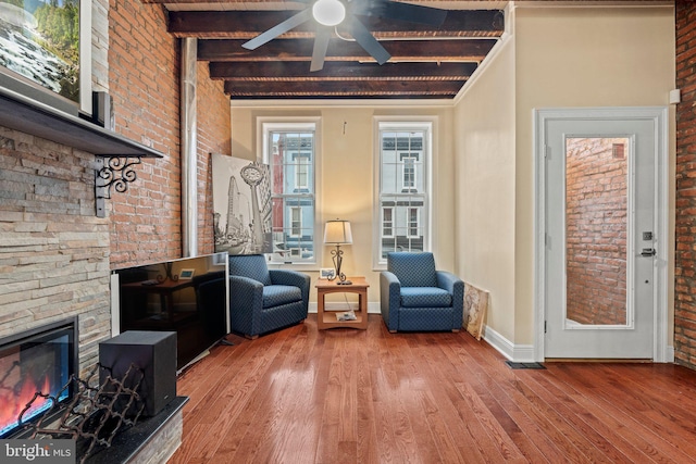 sitting room with beamed ceiling, wood-type flooring, brick wall, and a fireplace