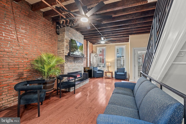 living room with hardwood / wood-style flooring, brick wall, a fireplace, and beamed ceiling