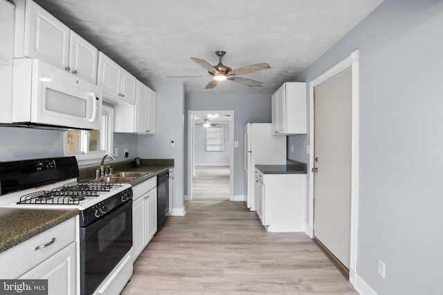 kitchen with white appliances, dark countertops, a sink, and white cabinets