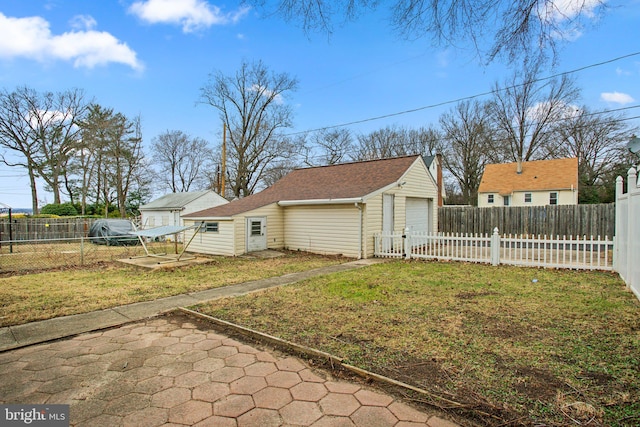 exterior space featuring an outbuilding, fence private yard, a shingled roof, a detached garage, and a lawn