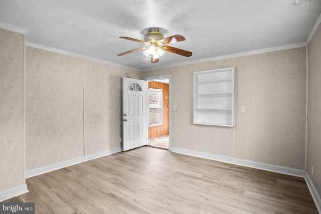 spare room with ceiling fan, built in shelves, wood finished floors, baseboards, and crown molding