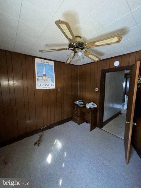 unfurnished room featuring ceiling fan and wood walls