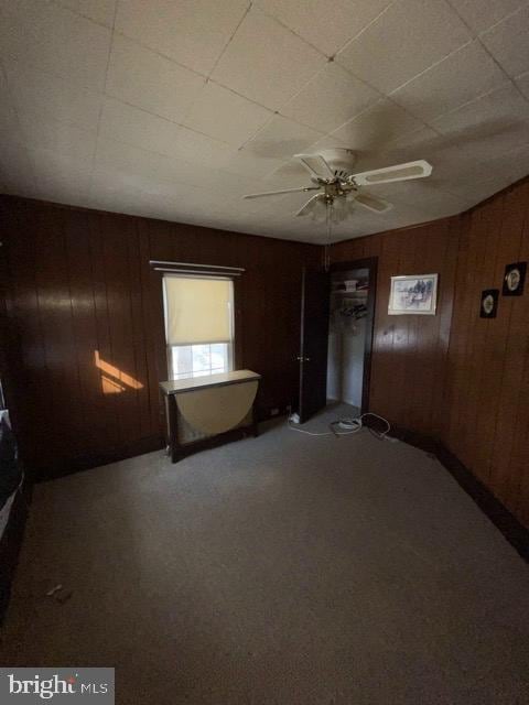 carpeted spare room featuring ceiling fan and wooden walls